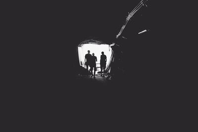 Tunnel showing light and three people at the end.