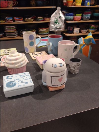 Many different types of pottery, including mugs, robots, containers and more, painted and ready to be fired.