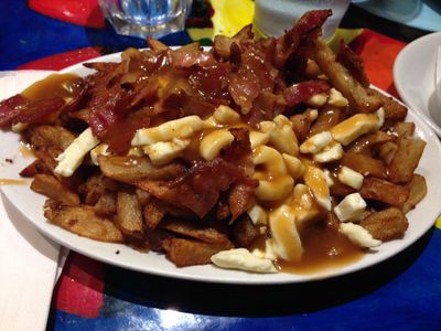 Plenty of poutine (fries, gravy, cheese curds and bacon) on a plate.